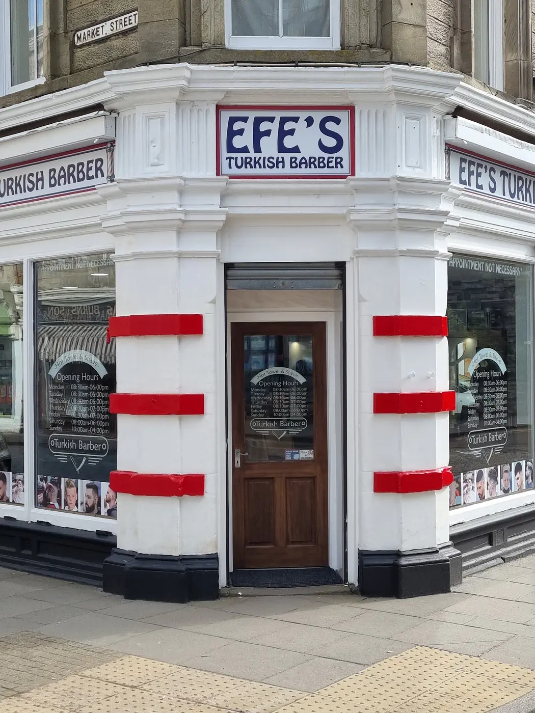 The corner shopfront of Efe's Turkish Barber, navy sign on white with red-striped pillars